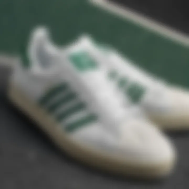 Close-up view of white Adidas shoes with green accents on a skateboard.